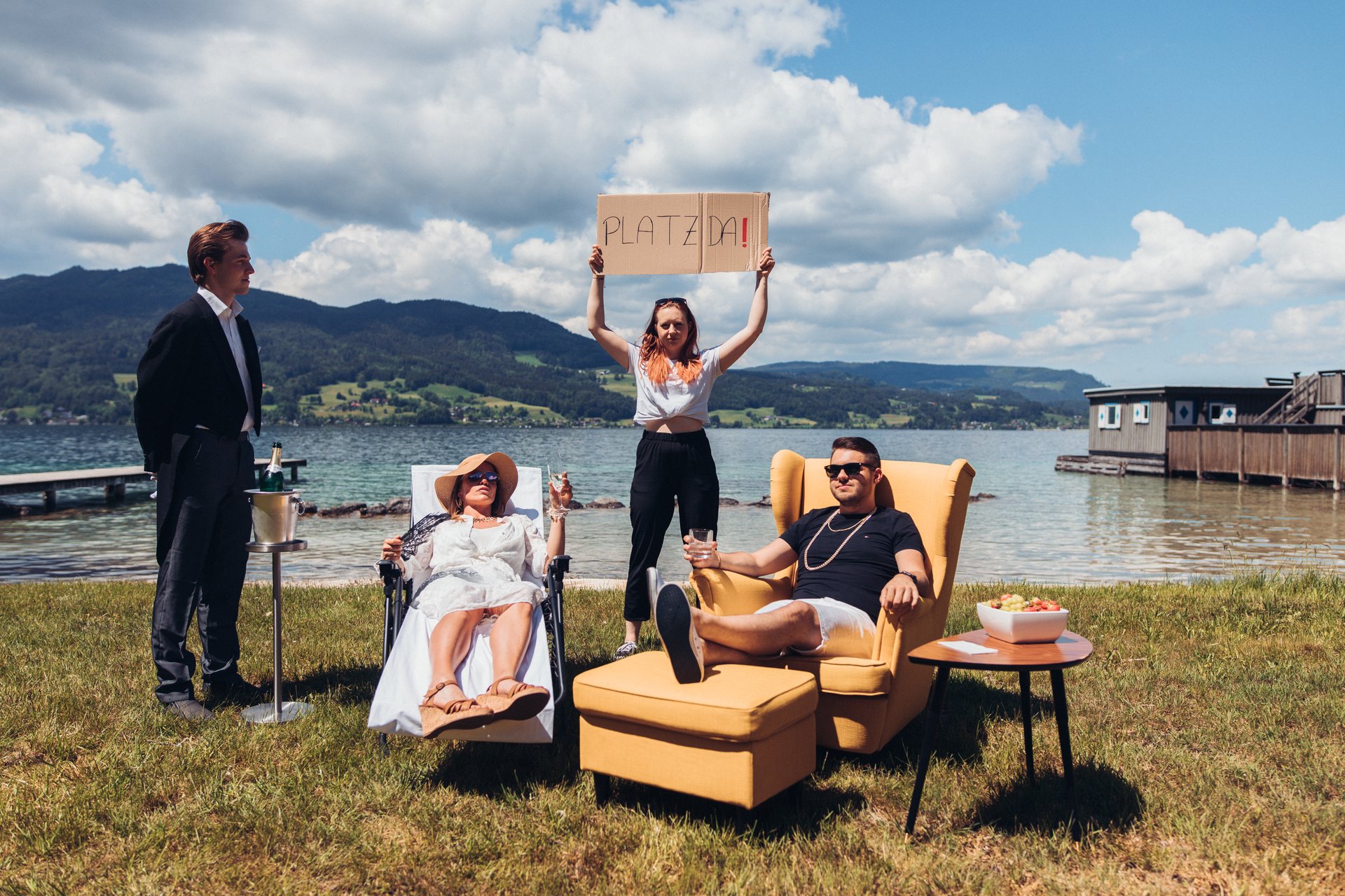 Reiche chillen am Attersee. Aktivistin hält im Hintergrund Schild mit SJ-Forderungen hoch