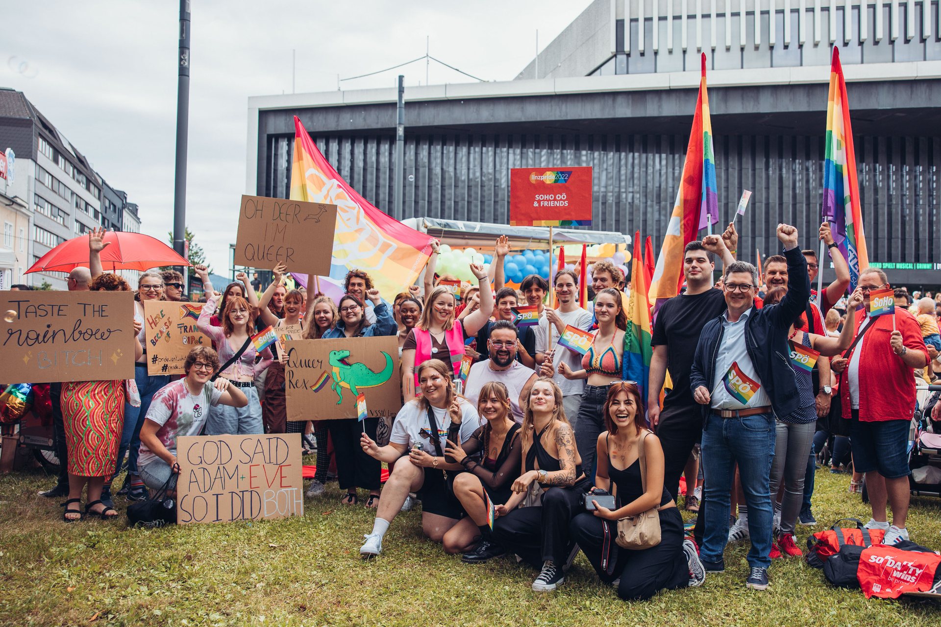Viele Menschen stehen für ein Gruppenfoto zusammen und tragen Regenbogenfahnen, Schilder mit Aufschriften wie "God said Adam plus Eva. So i did both."