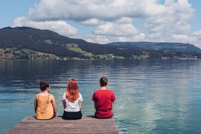 Jugendliche sitzen am Steg und blicken auf den Attersee