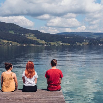 Jugendliche sitzen am Steg und blicken auf den Attersee