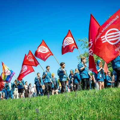 junge Menschen gehen im traditionellen SJ-Blauhemd gekleidet mit roten SJ-Fahnen