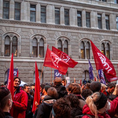 Demonstration. Die Straße ist voll mit Menschen, mehrere Fahnen sind zu sehen.