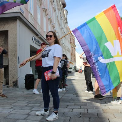 Frau hält eine Pride Fahne auf der Sozialistische Jugend Oberösterreich zu lesen ist.